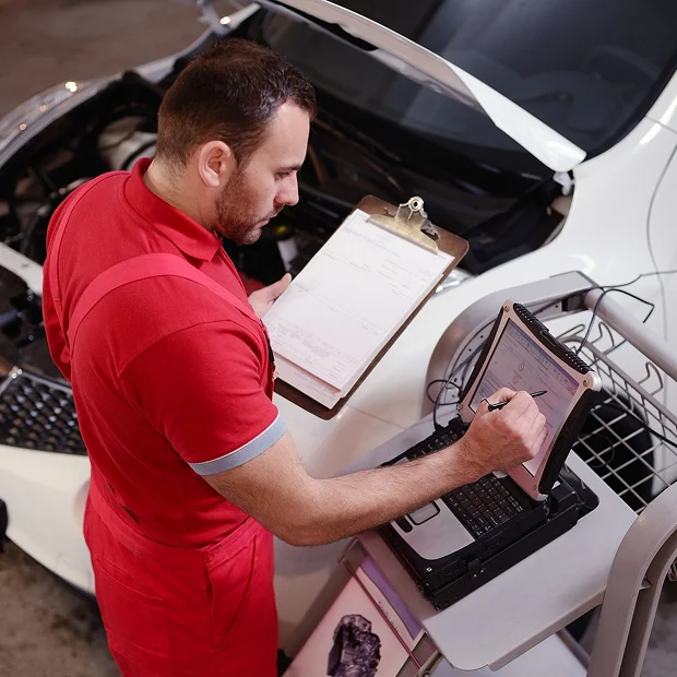 Mécanicien automobile en salopette rouge vérifiant un véhicule avec tablette et presse-papiers Les Essarts-le-Roi dans les Yvelines 78