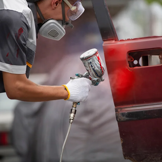 Un homme avec un masque et des lunettes peint une voiture rouge Les Essarts-le-Roi dans les Yvelines 78